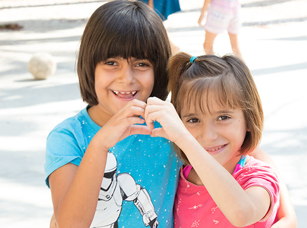 Dos niñas abrazadas haciendo el símbolo del corazón con sus manos